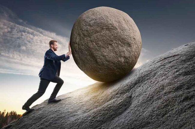 Business leader pushing a heavy boulder uphill, symbolizing structural challenges in emerging markets and the importance of Building Investor Confidence.