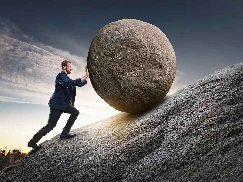 Business leader pushing a heavy boulder uphill, symbolizing structural challenges in emerging markets and the importance of Building Investor Confidence.