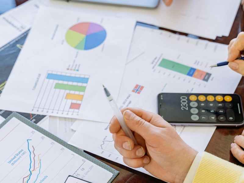 Close-up of hands reviewing colorful charts and financial data with a calculator on the desk, representing performance analysis and goal tracking.