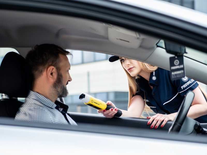 Driver in a car showing documents while a police officer holds a device during a roadside check.