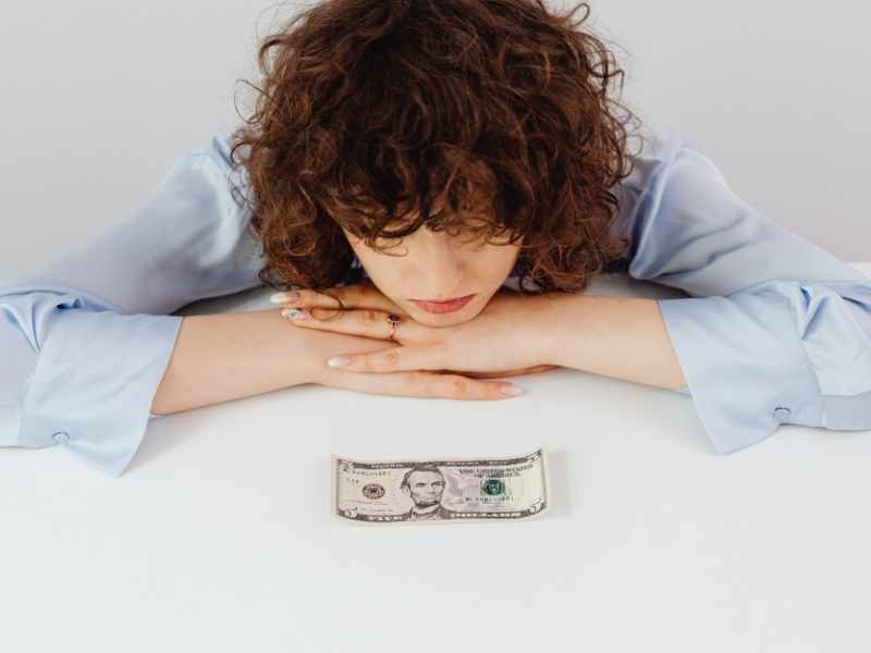 Person resting their head on a table with cash in front, showing financial stress and burnout.