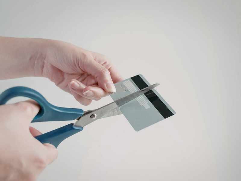 Hand cutting a credit card with scissors, symbolizing stopping overspending to accelerate debt payoff.