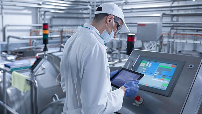 Industrial technician reviewing production data on a digital control panel inside a food processing facility.