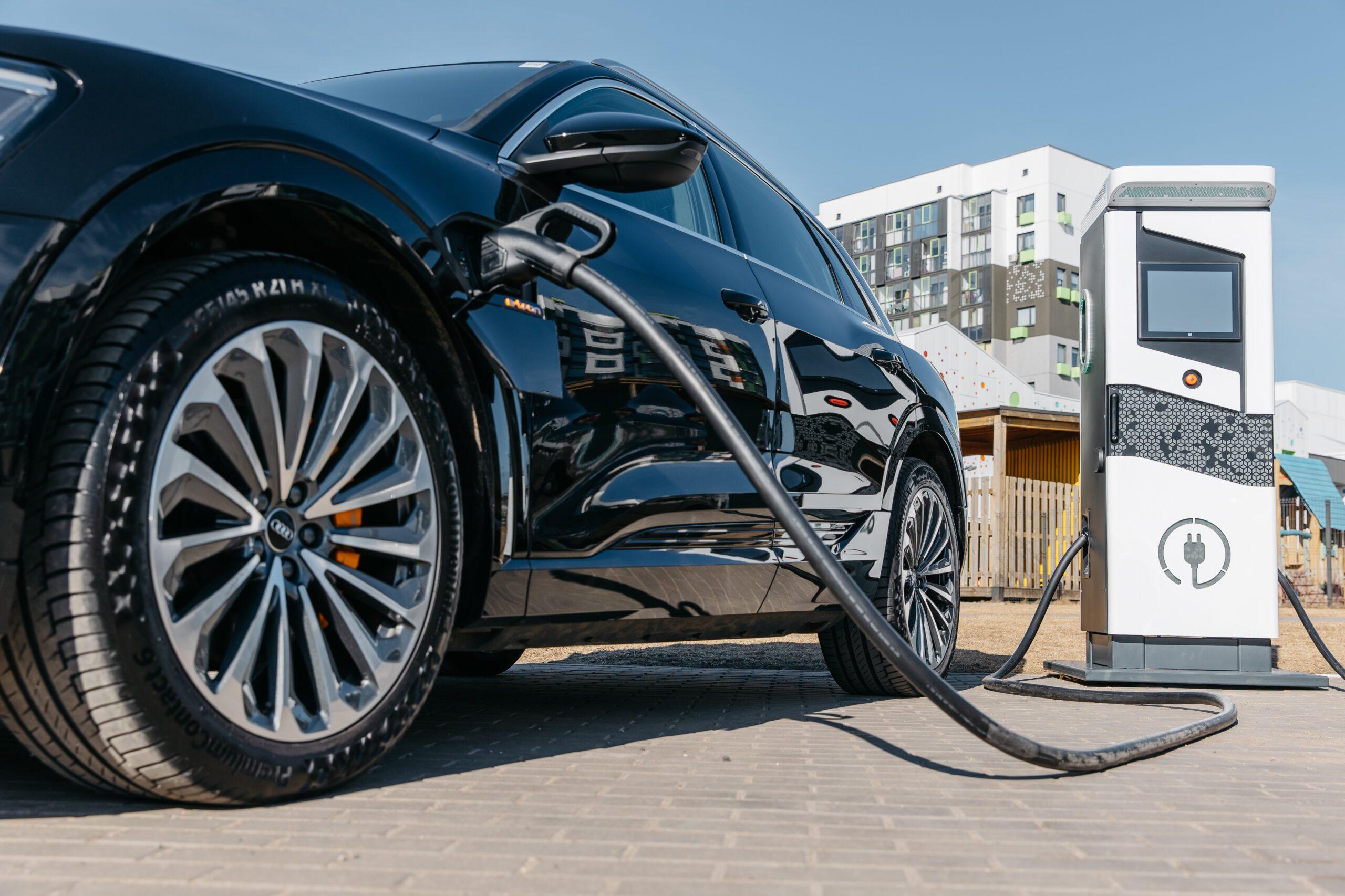 Electric vehicle connected to a public charging station in a parking area, illustrating infrastructure for electric mobility.